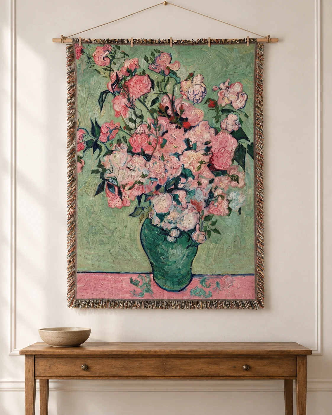 Pink flowers in a green vase on a woven tapestry above an antique wooden console