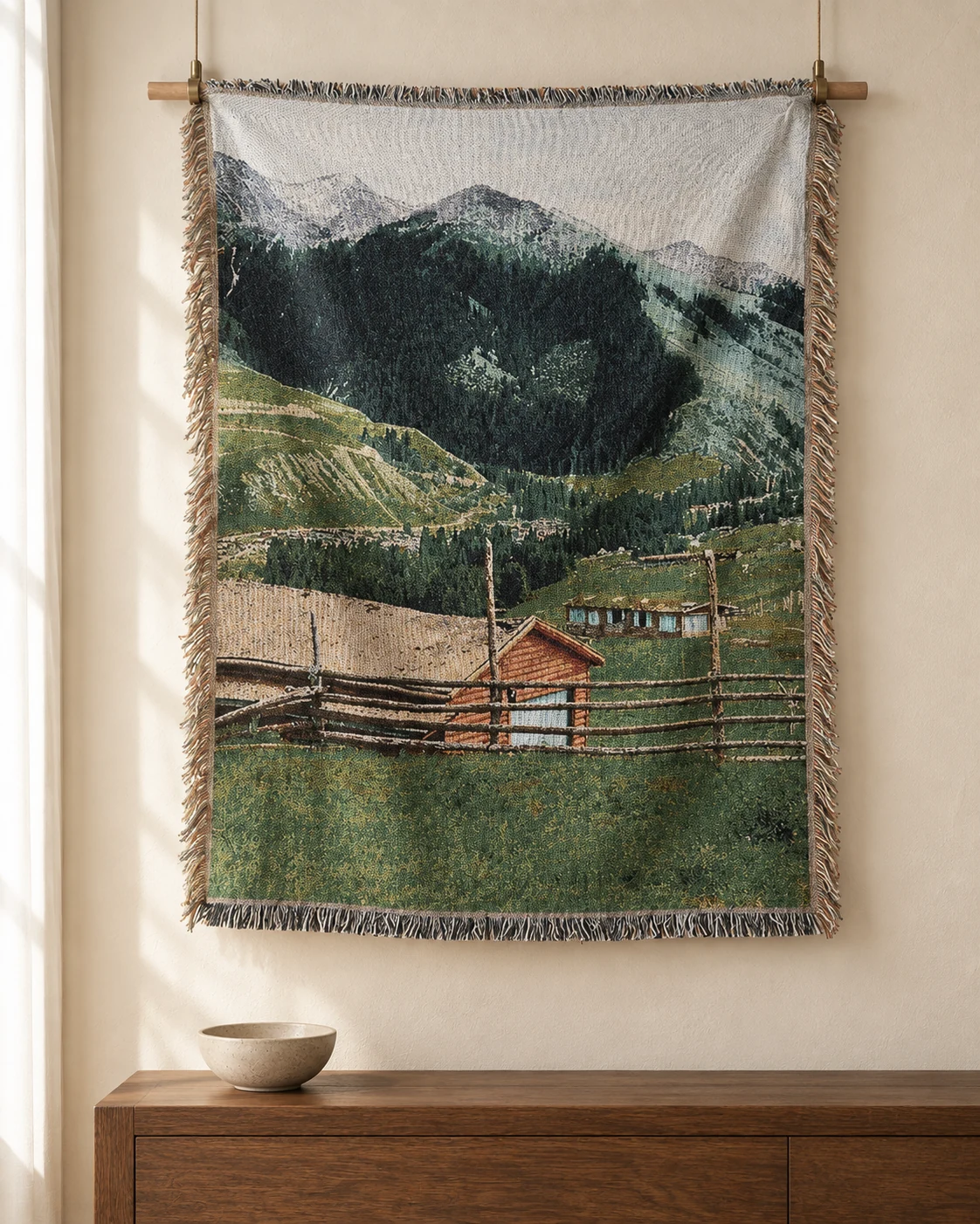A mountain cabin and wooden fence against forested hills on a woven tapestry