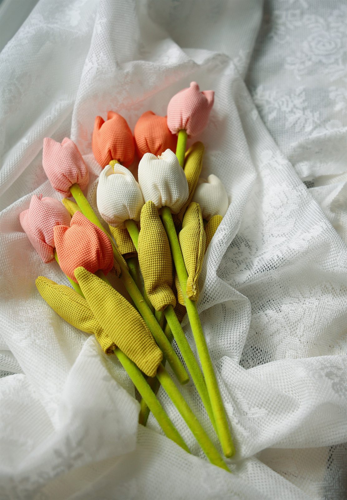 A bunch of soft yellow, orange and pink tulips resting on white fabric